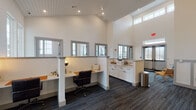 Hillson Business Lofts, located in Nashville, TN, is a thoughtfully designed coworking facility that blends professional functionality with an inspiring, creative atmosphere. The single-floor layout is anchored by dramatically vaulted ceilings clad in shiplap, which lend a loft-like character to the open workspace and fill the interior with an airy, expansive feel.

Natural light streams in through a generous array of clerestory and standard windows positioned along the perimeter, keeping the space bright and connected to the outdoors. The flooring throughout features a durable, textured carpet tile in a deep charcoal tone that grounds the crisp white walls and cabinetry.

The workspace is organized around multiple built-in workstations with warm wood desk surfaces and ergonomic seating, each defined by partial-height partitions that offer a degree of privacy without sacrificing the open, collaborative energy of the room. A dedicated coffee corner with white cabinetry and counter space provides a convenient amenity for occupants.

A welcoming reception area greets visitors at the entrance, complete with a sleek white front desk and pendant globe lighting. The entryway makes a bold first impression with a branded floor mat and a motivational mural — "Stay Hungry, Even If You Wear a Lot of Hats" — accompanied by a decorative hat display, reinforcing the entrepreneurial spirit that defines Hillson Business Lofts.