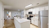 Located at Cameron Woods Dr in Apex, NC, this 2-bedroom, 2-bathroom single-floor residence offers a thoughtfully designed open-concept layout. The combined kitchen, dining, and living area serves as the heart of the home, featuring a large white quartz island with a built-in sink, crisp white cabinetry, a subway tile backsplash, and stainless steel appliances. Light wood-style flooring runs throughout the main living areas, lending a clean, cohesive aesthetic. The living room is bright and welcoming, with a ceiling fan, large windows, and a glass patio door that fills the space with natural light and provides access to a private patio with wooded views. The primary bedroom is a comfortable retreat with plush carpet, multiple windows overlooking the outdoors, and ample closet space. The second bedroom is equally well-appointed. Both bathrooms are finished in light, neutral tones with wood-look flooring and tub-shower combinations. A dedicated laundry room houses a full-size washer and dryer. Additional conveniences include a pantry, utility room, and three closets. The overall ambiance is bright, modern, and functional, ideal for everyday living.