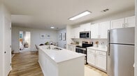 Located at Cameron Woods Dr in Apex, NC, this 2-bedroom, 2-bathroom single-floor residence offers a thoughtfully designed open-concept layout. The combined kitchen, dining, and living area serves as the heart of the home, featuring a large white quartz island with a built-in sink, crisp white cabinetry, a subway tile backsplash, and stainless steel appliances. Light wood-style flooring runs throughout the main living areas, lending a clean, cohesive aesthetic. The living room is bright and welcoming, with a ceiling fan, large windows, and a glass patio door that fills the space with natural light and provides access to a private patio with wooded views. The primary bedroom is a comfortable retreat with plush carpet, multiple windows overlooking the outdoors, and ample closet space. The second bedroom is equally well-appointed. Both bathrooms are finished in light, neutral tones with wood-look flooring and tub-shower combinations. A dedicated laundry room houses a full-size washer and dryer. Additional conveniences include a pantry, utility room, and three closets. The overall ambiance is bright, modern, and functional, ideal for everyday living.