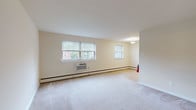 This single-floor residence offers a practical and comfortable layout designed to maximize functionality across its living spaces. The open living and dining area is generously proportioned, finished with neutral-toned carpet and cream walls that create a bright, welcoming atmosphere. Multiple windows fitted with horizontal blinds allow natural light to fill the space while providing views of surrounding greenery. Baseboard heating runs along the perimeter, and a wall-mounted air conditioning unit ensures year-round comfort.

The kitchen is accessible directly from the living area and features light wood cabinetry, dark granite-style countertops, a tile backsplash, and light hardwood flooring. White appliances — including a gas range, over-the-range microwave, and full-size refrigerator — provide a complete cooking setup alongside a stainless steel sink.

The bedrooms are carpeted and well-proportioned, each with a window offering outdoor views, baseboard heating, and a wall AC unit. The bathroom is finished in clean white tile, featuring a full soaking tub with chrome fixtures, a single vanity with under-sink storage, a mirrored medicine cabinet, and tile flooring — maintaining a consistent, tidy aesthetic throughout.