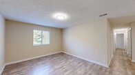 Located at 10920 Covington Bypass Rd in Covington, GA, this single-floor, three-bedroom, two-bathroom home offers a practical and comfortable layout with consistent neutral tones throughout. The kitchen features white cabinetry, light laminate countertops, a double stainless steel sink, and white appliances including a range and refrigerator, all set atop wood-look luxury vinyl flooring that extends through the main living areas. The space opens to a generously sized adjoining area, providing ample room for dining or additional living arrangements. The primary bedroom is notably spacious, featuring soft carpeting, a window with outdoor views, and access to a walk-in closet equipped with dual wire shelving systems for organized storage. The additional bedrooms are also carpeted and well-sized, each with windows allowing natural light. Both bathrooms include full tub-shower combinations with clean white surrounds and brushed nickel hardware. A dedicated laundry room with washer and dryer hookups adds everyday convenience. Textured ceilings are present throughout, and the overall palette of warm beige walls and light flooring creates a bright, cohesive ambiance across the entire home.