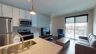 Located on North High Street in Columbus, Ohio, this modern unit offers a thoughtfully designed open-concept layout that seamlessly connects the kitchen and living area. The kitchen is a standout feature, equipped with stainless steel appliances including a refrigerator, electric range, and over-the-range microwave. White shaker-style cabinetry with sleek hardware pairs beautifully with a light granite countertop, while a subway tile backsplash adds a contemporary touch. A central island with an undermount sink, pendant lighting overhead, and bar seating makes it ideal for both cooking and casual dining. Rich hardwood-style flooring flows throughout the main living space, lending warmth and continuity to the interior. The living area is bright and inviting, anchored by a large sliding glass door that opens to a private balcony, offering elevated views of the surrounding Columbus neighborhood and skyline. The bathroom is clean and functional, featuring a glass-enclosed shower, hardwood-style flooring, and crisp white finishes. Neutral wall tones and modern fixtures throughout contribute to a cohesive, contemporary aesthetic. The space is efficiently organized, with a closet providing convenient storage. Overall, this unit combines practical design with modern finishes in a prime Columbus location.