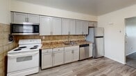 Located at 53 Crawford St in Eatontown, NJ, this single-floor residence offers a well-organized layout designed for comfortable everyday living. The kitchen is a standout feature, equipped with gray shaker-style cabinetry, granite-look countertops, a tile backsplash, and stainless steel appliances including a dishwasher and refrigerator, complemented by a white electric range and built-in microwave. Light wood-look flooring runs throughout the kitchen, adding a clean, modern touch. The living area is generously proportioned, featuring neutral-toned carpet, warm beige walls, and crown molding that lends a classic finish. A large window allows natural light to fill the room while providing views of the surrounding greenery, and a wall-mounted HVAC unit ensures year-round comfort. The bedrooms continue the warm, neutral palette with plush carpeting, white trim, and multiple windows that brighten the spaces naturally, along with baseboard heating. The bathroom is finished with white tile flooring, a full tub and shower combination with marble-style wall surrounds, and a clean white vanity. Overall, the space presents a practical and inviting atmosphere suited for a variety of lifestyles.