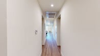 Located on Fountain Avenue in the heart of Los Angeles, this modern single-floor unit offers four bedrooms and four bathrooms with a clean, contemporary design throughout. The kitchen serves as a standout feature, showcasing floor-to-ceiling gray cabinetry, stainless steel appliances including a gas range, built-in microwave, and a full-size refrigerator, all anchored by a striking marble-topped island that doubles as a dining area. Light wood-style flooring runs seamlessly throughout the unit, complementing the crisp white walls and recessed lighting that create a bright, airy atmosphere. A long, well-lit hallway connects the bedrooms, each offering a compact yet functional layout. Several bedrooms feature large sliding windows that invite natural light and provide views of the surrounding Los Angeles neighborhood. The four bathrooms vary in design — some feature modern vanities with mirrored medicine cabinets and large-format tile flooring, while at least one includes a glass-enclosed walk-in shower with elegant marble-style tile surround. The overall aesthetic is minimalist and contemporary, with consistent finishes and neutral tones creating a cohesive living environment suited for shared or multi-occupant living in a vibrant urban setting.