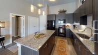 This single-story residence on Harmony Hill Lane in Rowlett, Texas, presents a thoughtfully designed interior with contemporary finishes throughout. The kitchen serves as a central highlight, featuring dark espresso-toned cabinetry, granite countertops, a tile backsplash, and black appliances. A large island with bar seating and pendant lighting overhead creates an ideal space for both meal preparation and casual dining. Wood-style flooring flows consistently throughout the home, adding warmth and visual continuity.

The living area offers a cozy yet stylish atmosphere with large windows that bring in natural light. Multiple bedrooms provide versatile accommodation, each with generous windows dressed with panel curtains. One bedroom features a bold accent wall and direct access to an en suite bathroom equipped with a glass-enclosed walk-in shower. A second full bathroom includes a soaking tub with tile surround and granite vanity. A dedicated home office is outfitted with built-in shelving and a large work surface, ideal for productivity. Additional highlights include a spacious walk-in closet with multi-tier shelving and hanging rods, completing this well-appointed home.