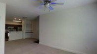 This single-floor space offers a clean and functional layout designed for comfortable everyday living. The main living area is generously sized, featuring soft carpet flooring that adds warmth underfoot and neutral-toned walls that create a bright, open atmosphere. A ceiling fan with a light fixture is centrally mounted overhead, providing both air circulation and ambient lighting throughout the room.

An open hallway or passageway connects the main living area to additional rooms beyond, offering a sense of flow and connectivity throughout the floor plan. Visible in the background are built-in shelving or cabinetry elements, suggesting organized storage solutions and thoughtful use of space. The arched or curved transition between spaces adds a subtle architectural detail that softens the overall aesthetic.

The space presents a straightforward, livable environment with a neutral palette that lends itself well to a variety of interior styles. The layout appears practical and well-proportioned, with each area transitioning smoothly into the next. Overall, this single-level space combines simple, functional design with comfortable finishes, making it a versatile and approachable living environment.