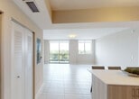 Located at 28250 S Dixie Hwy in Homestead, Florida, this single-floor residence offers a clean, contemporary design throughout. The open-concept living area is finished with large-format white tile flooring and features floor-to-ceiling sliding glass doors that lead to a private balcony, filling the space with natural light and providing sweeping views of the surrounding greenery and skyline.

The kitchen is a standout feature, outfitted with light wood cabinetry, sleek light-colored countertops, a subway tile backsplash, stainless steel sink, and black appliances including a refrigerator, dishwasher, and range. A central island with seating makes it ideal for casual dining and entertaining.

The bedrooms are bright and airy, each featuring light wood-style tile flooring, ceiling fans, and large windows that capture panoramic outdoor views and abundant natural light. The neutral warm-toned walls create a calm, welcoming atmosphere throughout.

The bathrooms are finished with modern fixtures and light wood vanities topped with white countertops. One bathroom includes a walk-in shower, while another offers a full soaking tub with tiled surround. The entry foyer includes louvered closet doors, adding functional storage while maintaining the home's cohesive contemporary aesthetic.