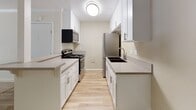 Located at 16031 Pioneer Blvd in Norwalk, California, this single-floor unit offers a well-designed layout that maximizes functionality throughout. The kitchen is a standout feature, finished with crisp white shaker cabinetry, light stone-toned countertops, and a full suite of stainless steel appliances including a gas range, microwave, and refrigerator. Light wood-look flooring runs through the kitchen, adding warmth and easy maintenance to the space. A peninsula with a breakfast bar connects the kitchen to the living area, which transitions to plush carpeting and features crown molding, a ceiling fan, and a textured ceiling. The open-concept flow between the kitchen and living room creates a spacious, airy feel that is ideal for everyday living. A bedroom offers carpeted flooring, a wall-mounted air conditioning unit, and a window with vertical blinds that brings in natural light and garden views. An additional carpeted room with a window overlooking mature trees provides flexible use as a second bedroom or office. The bathroom is clean and functional, complete with a tub-shower combo, a white vanity with stone-topped counters, and wood-look tile flooring. Throughout the unit, a neutral color palette and consistent finishes create a cohesive and move-in-ready environment.