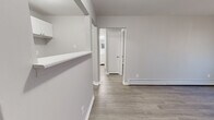 Located at 3583 Alaska Ave in Cincinnati, Ohio, this single-level one-bedroom, one-bathroom unit offers a clean, modern aesthetic achieved through fresh neutral gray paint, crisp white trim, and consistent wood-look laminate flooring throughout. The layout is efficiently organized, connecting each room through a central hallway that provides a logical flow across the space.

The living area is bright and open, featuring a wall-mounted air conditioning unit and a baseboard heating system, with natural light filtering in through a window fitted with blinds. The kitchen is thoughtfully appointed with white cabinetry, granite-look countertops, a stainless steel single-basin sink, and upper cabinets offering practical storage. A half-wall peninsula detail adds architectural interest while separating the kitchen from the main living area.

The bedroom is a comfortably sized retreat with neutral gray walls, wood-look flooring, a window with blinds for natural light and privacy, and a baseboard heater. The bathroom is finished in a clean, classic style, featuring a full-size bathtub with a tiled surround in white, complemented by chrome fixtures. A white vanity with storage completes the bathroom.

Overall, the space presents a cohesive, move-in-ready environment with a clean, minimalist character well-suited for straightforward, comfortable single-occupant living.