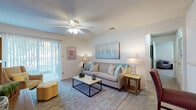 Located at 5577 Houston Road in Macon, Georgia, this 2-bedroom, 2-bathroom apartment model presents a thoughtfully designed single-story floor plan ideal for comfortable everyday living. The living room serves as the heart of the home, featuring plush carpeting, a ceiling fan with light fixture, and sliding glass doors that open to a private patio, allowing natural light to fill the space. The open-concept layout connects the living area seamlessly to the kitchen, which is equipped with warm wood cabinetry, a double-basin sink, and a pass-through bar that overlooks the adjoining dining room. The dedicated dining area is an intimate space accented by a chandelier overhead. Both bedrooms are generously sized with soft carpeting, ceiling fans, and windows that bring in natural light. Each room offers a calm, neutral palette throughout. The two full bathrooms feature warm wood vanities, tile flooring, and tub-shower combinations, providing functional and clean spaces. With a consistent color scheme of warm neutrals and light tones carried throughout, this apartment delivers a cohesive, welcoming ambiance suited for a variety of lifestyles.