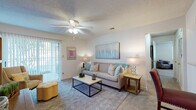 Located at 5577 Houston Road in Macon, Georgia, this 2-bedroom, 2-bathroom apartment model presents a thoughtfully designed single-story floor plan ideal for comfortable everyday living. The living room serves as the heart of the home, featuring plush carpeting, a ceiling fan with light fixture, and sliding glass doors that open to a private patio, allowing natural light to fill the space. The open-concept layout connects the living area seamlessly to the kitchen, which is equipped with warm wood cabinetry, a double-basin sink, and a pass-through bar that overlooks the adjoining dining room. The dedicated dining area is an intimate space accented by a chandelier overhead. Both bedrooms are generously sized with soft carpeting, ceiling fans, and windows that bring in natural light. Each room offers a calm, neutral palette throughout. The two full bathrooms feature warm wood vanities, tile flooring, and tub-shower combinations, providing functional and clean spaces. With a consistent color scheme of warm neutrals and light tones carried throughout, this apartment delivers a cohesive, welcoming ambiance suited for a variety of lifestyles.