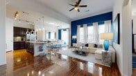 This two-floor residence makes a striking visual statement through its open-concept main living area, where bold cobalt blue accent walls contrast with crisp white trim and gleaming hardwood floors. The living room is spacious and bright, with multiple windows dressed in sheer white curtains that allow generous natural light to fill the space. A ceiling fan overhead and a large sectional sofa anchor the room, which flows seamlessly into the dining area. The dining space features the same dramatic blue walls, a glass-top table with white upholstered chairs, and a decorative mirror that amplifies the sense of space.

The kitchen is well-appointed with dark espresso cabinetry, granite countertops, stainless steel appliances, and a peninsula with bar seating. A primary bathroom offers dual sinks set into matching granite countertops with dark cabinetry below, while a secondary bathroom features a pedestal sink, wood-look flooring, and a tub-shower combination.

The bedrooms provide a calming retreat; the primary bedroom features soft neutral tones and plush carpet, while a secondary bedroom offers carpeted floors and ample natural light. Throughout, crown molding and consistent finishes lend a cohesive, polished character to the entire home.