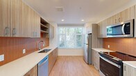 Located at 9950 NE Gibbs Dr in Hillsboro, Oregon, this three-story home offers a well-organized layout spread across three distinct levels. The ground floor houses an attached garage with an automatic opener, concrete flooring, and exposed ductwork overhead, along with an entrance that leads into the home. The main living level features a bright, open living room with light wood flooring, crisp white walls, and dual windows that invite natural light and views of the surrounding neighborhood. The galley-style kitchen is thoughtfully designed with warm wood cabinetry, open shelving, light quartz countertops, a tile backsplash, and stainless steel appliances including a refrigerator, range, microwave, and dishwasher. A large window at the end of the kitchen frames a verdant outdoor view. A pantry provides additional storage, and a hallway with wood flooring connects the rooms efficiently. The upper floors accommodate three bedrooms, each featuring light wood floors and closets with sliding doors and built-in shelving. Four bathrooms are distributed throughout the home, including clean, minimalist designs with wood vanities, walk-in showers with white tile surrounds, and natural light from windows. A dedicated laundry area and multiple staircases with carpeted treads complete this practical and modern multi-level home.