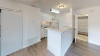 This single-floor residence offers a clean, functional layout designed for comfortable everyday living. The living area welcomes you with durable wood-look flooring, bright white walls, and multiple windows that bring in natural light and views of the surrounding exterior. A ceiling fan adds to the room's airy feel, while a dedicated entryway door provides a welcoming point of entry.

The kitchen is thoughtfully designed in a galley-style configuration and features white cabinetry with ample storage, light speckled countertops, a stainless steel double-basin sink, and white appliances including an electric range, oven, and refrigerator. A peninsula with a matching countertop separates the kitchen from the living space, creating an open-concept flow ideal for everyday use and casual dining.

The bedrooms are generously sized with soft neutral carpeting, white walls, and windows that allow natural light to filter in. The primary bedroom includes a mirrored sliding closet and connects to an adjoining room or bathroom corridor, enhancing its functionality.

The bathroom is finished with light tile flooring, a full tub-shower combination, a toilet, and a dark-cabinetry vanity with a clean white countertop. The overall aesthetic throughout the space is neutral and understated, offering a versatile, move-in-ready canvas.