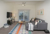This 4-bedroom, 2-bathroom unit is thoughtfully designed across a single floor, offering a functional and modern living environment well-suited for shared occupancy. The open-concept common area seamlessly integrates the kitchen and living space, creating a communal hub that feels both spacious and inviting. The kitchen is outfitted with stainless steel appliances, including a full-size refrigerator, and features a clean two-tone cabinet design with white upper cabinets and dark lower cabinets, complemented by light wood-look luxury vinyl plank flooring that flows throughout the space. Recessed lighting and a ceiling fan enhance both comfort and illumination in the living area, which includes room for a sofa, coffee table, and entertainment setup. A sliding glass door with vertical blinds allows natural light to fill the space while providing outdoor access. Each bedroom is comfortably sized to accommodate a full or queen bed, a desk, and personal storage. The bedrooms feature vertical blind-covered windows or sliding glass doors that invite natural light, with neutral walls that offer a versatile backdrop. The overall ambiance is clean, contemporary, and practical, designed to support a comfortable day-to-day lifestyle.