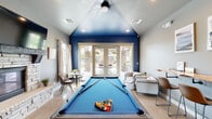 Located at 1465 W. Deer Crest Dr. in Meridian, Idaho, this single-story community clubhouse offers a well-rounded collection of amenity spaces designed for recreation, fitness, and socializing. The building's layout encompasses several distinct areas, each thoughtfully appointed to serve a specific purpose.

The centerpiece of the clubhouse is a vibrant game room featuring a full-size pool table with blue felt set beneath a vaulted ceiling accented with bold blue paint. French doors along the back wall invite abundant natural light and provide views of the surrounding community. A live-edge wood bar counter with leather barstools lines one wall, while framed artwork and seating areas complete the relaxed, social atmosphere.

Adjacent to the game room, a cozy lounge nook offers a round marble-top table flanked by upholstered chairs, positioned beside a large window overlooking landscaped grounds and a stacked-stone fireplace surround.

The fitness center is generously sized and well-lit, featuring recessed lighting, ceiling fans, and multiple windows. It is equipped with treadmills, an elliptical, a stationary bike, and a cable resistance machine, along with wall-mounted televisions and organized storage.

Outside, a covered patio with a wood-plank ceiling and stacked-stone columns provides a comfortable gathering space with high-top seating and open views of the community streetscape.