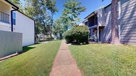 Located at 300 Hickory Ridge Cir in Hopkinsville, Kentucky, this property offers a welcoming outdoor environment defined by its thoughtfully maintained grounds and natural surroundings. The exterior features classic residential buildings with white and gray siding, gabled rooflines, and upper-level balconies with metal railings, presenting a traditional architectural style.

The grounds are a standout feature of this property. Expansive, well-kept lawns stretch between the buildings, shaded by a generous canopy of mature deciduous and evergreen trees. These trees not only provide ample shade but also lend the property a serene, park-like atmosphere. Concrete walkways wind throughout the grounds, offering clean pedestrian pathways connecting the buildings and outdoor areas.

Landscaping details include neatly trimmed shrubs along building foundations, decorative rock arrangements, and mulched planting beds that add visual interest and texture. Open green spaces between structures create a sense of openness and room to breathe. The surrounding area offers open views of adjacent fields and sky, further enhancing the tranquil character of the setting.

Ground-level units feature private patio areas with fenced enclosures, while upper units enjoy elevated balconies overlooking the lush greenery below. The overall ambiance is calm and residential, with abundant natural light, greenery, and a well-organized layout that makes the most of the property's outdoor spaces.