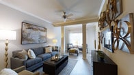 Located at 45 Lullwater Dr in Richmond Hill, Georgia, this single-story residence offers a thoughtfully designed layout with refined interior details and a welcoming ambiance. The living area serves as the heart of the home, showcasing elegant crown molding, decorative columns, and smooth ceilings accented by a ceiling fan — details that lend a sense of architectural character and craftsmanship. The space flows seamlessly into a secondary sitting area, defined by the columned divide, allowing for flexible use of the open floor plan. Large windows dressed with sheer curtains invite an abundance of natural light, creating a bright and airy atmosphere throughout. The hard-surface flooring adds both durability and visual continuity across the living spaces. Neutral wall tones paired with warm accent lighting contribute to a comfortable and polished aesthetic. Wall art and curated décor elements enhance the overall sense of style, reflecting a home that balances practicality with thoughtful design. The single-floor layout ensures ease of access and convenient living throughout, making this Richmond Hill property a well-appointed and inviting place to call home.