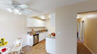 Located at 7860 Valley View St in Buena Park, California, this single-floor unit offers a practical and well-organized layout designed for comfortable everyday living. The kitchen is a standout feature, outfitted with crisp white shaker-style cabinetry, granite-look countertops, a stainless steel dishwasher, and a pass-through counter that connects to the dining area. Wood-look flooring runs throughout the kitchen, adding warmth and durability to the space. A galley-style extension provides additional counter space and storage, making the kitchen highly functional. The open living area is generously sized, finished with neutral-toned carpet and warm beige walls that create a calm, welcoming atmosphere. A wall-mounted air conditioning unit ensures year-round comfort. The bedrooms are carpeted and offer ample space, with one room featuring a sliding closet and another benefiting from a window that allows natural light and outdoor views. The bathroom is thoughtfully appointed with a wide vanity, granite-look countertop, white cabinetry, and a large mirror with overhead lighting. Clean white trim and neutral paint tones are carried consistently throughout the unit, contributing to a cohesive and tidy aesthetic overall.