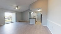 This single-floor residence offers a thoughtfully designed open-concept layout that seamlessly connects the living area to the kitchen. The living space features light wood-look flooring, vaulted ceilings, and a ceiling fan, creating an airy and comfortable atmosphere. Sliding glass doors lead to a private balcony, inviting an abundance of natural light and outdoor views. The kitchen is well-equipped with stainless steel appliances, white cabinetry, a white subway tile backsplash, dark countertops, and a peninsula that doubles as a breakfast bar — all complemented by pendant lighting overhead. The bedrooms are carpeted for warmth and comfort, each featuring ceiling fans and windows that frame views of lush greenery. One bedroom boasts notably tall ceilings, adding a sense of grandeur to the space. The two bathrooms are finished in a clean, modern style with white cabinetry, dark countertops, tile flooring, and full tub-shower combinations. Throughout, soft gray walls provide a neutral and cohesive palette, while consistent brushed nickel hardware adds a polished touch. The overall ambiance is bright, clean, and move-in ready.
