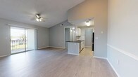 This single-floor residence offers a thoughtfully designed open-concept layout that seamlessly connects the living area to the kitchen. The living space features light wood-look flooring, vaulted ceilings, and a ceiling fan, creating an airy and comfortable atmosphere. Sliding glass doors lead to a private balcony, inviting an abundance of natural light and outdoor views. The kitchen is well-equipped with stainless steel appliances, white cabinetry, a white subway tile backsplash, dark countertops, and a peninsula that doubles as a breakfast bar — all complemented by pendant lighting overhead. The bedrooms are carpeted for warmth and comfort, each featuring ceiling fans and windows that frame views of lush greenery. One bedroom boasts notably tall ceilings, adding a sense of grandeur to the space. The two bathrooms are finished in a clean, modern style with white cabinetry, dark countertops, tile flooring, and full tub-shower combinations. Throughout, soft gray walls provide a neutral and cohesive palette, while consistent brushed nickel hardware adds a polished touch. The overall ambiance is bright, clean, and move-in ready.
