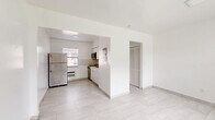 Located at 2030 NE 162nd St in North Miami Beach, FL, this single-floor unit offers a clean, minimalist design throughout. Light-toned large-format tile flooring runs continuously across the space, enhancing the sense of openness and reflecting natural light from multiple windows fitted with blinds.

The living area is open and airy, characterized by crisp white walls and a straightforward layout that connects seamlessly to the kitchen via an arched passthrough opening. The kitchen is well-appointed with white cabinetry, a subtle tile backsplash, stainless steel appliances including a full-size refrigerator, a stove, and an over-the-range microwave, as well as a single-basin sink with a window above it providing natural light and ventilation.

The bathroom is finished in all-white tile with a shower-tub combination, a window for natural light, and a white vanity, maintaining the clean and uniform aesthetic found throughout the unit. Two closets provide practical storage solutions, while an additional unclassified room offers flexible use. A windowed entry room with a paneled door leads to the exterior, completing the functional layout of this well-maintained North Miami Beach residence.