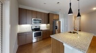 Located at 1106 Scenic Club Dr. in Cary, NC, this well-appointed single-floor residence combines modern design with functional living. The open-concept layout connects the kitchen and living areas seamlessly, creating a bright and cohesive space bathed in natural light from multiple windows. The kitchen is a standout feature, equipped with rich dark wood cabinetry extending to the ceiling, granite countertops, a large central island with a sink and stylish pendant lighting, and a full suite of stainless steel appliances including a range, microwave, and French door refrigerator. Warm hardwood-style flooring runs throughout the main living areas, adding a sense of warmth and continuity. The living room is generously proportioned, featuring a ceiling fan and ample natural light. The bedrooms are carpeted for comfort, each with ceiling fans and windows overlooking the surrounding community. The bathrooms are finished to a high standard, showcasing granite-topped dark wood vanities—one with dual sinks—hardwood-style flooring, and well-lit mirrors. The overall aesthetic throughout is clean and contemporary, with neutral tones, white trim, and modern fixtures creating a cohesive, move-in-ready environment.