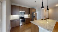 Located at 1106 Scenic Club Dr. in Cary, NC, this well-appointed single-floor residence combines modern design with functional living. The open-concept layout connects the kitchen and living areas seamlessly, creating a bright and cohesive space bathed in natural light from multiple windows. The kitchen is a standout feature, equipped with rich dark wood cabinetry extending to the ceiling, granite countertops, a large central island with a sink and stylish pendant lighting, and a full suite of stainless steel appliances including a range, microwave, and French door refrigerator. Warm hardwood-style flooring runs throughout the main living areas, adding a sense of warmth and continuity. The living room is generously proportioned, featuring a ceiling fan and ample natural light. The bedrooms are carpeted for comfort, each with ceiling fans and windows overlooking the surrounding community. The bathrooms are finished to a high standard, showcasing granite-topped dark wood vanities—one with dual sinks—hardwood-style flooring, and well-lit mirrors. The overall aesthetic throughout is clean and contemporary, with neutral tones, white trim, and modern fixtures creating a cohesive, move-in-ready environment.