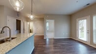Located at 2460 Walcutt Rd in Columbus, Ohio, this single-floor residence offers a thoughtfully designed open-concept layout that seamlessly connects the kitchen, dining, and living areas. The kitchen is a standout feature, outfitted with sleek gray shaker-style cabinetry, granite countertops, a classic white subway tile backsplash, and a full suite of stainless steel appliances including a range, over-the-range microwave, and refrigerator. A peninsula with an undermount sink and pendant lighting above adds both function and visual appeal. Rich wood-style plank flooring extends throughout the main living areas, providing a warm, cohesive aesthetic. The open living space is bright and well-proportioned, with multiple doorways leading to additional rooms. The bedroom features plush carpeting and a generously sized window that allows natural light to fill the room while offering outdoor views. The bathroom is finished with gray cabinetry, a white countertop, wood-look tile flooring, and brushed nickel hardware and fixtures. Throughout the unit, neutral warm-gray walls, white trim, and modern finishes create a clean, contemporary ambiance that is both practical and inviting.
