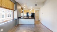 Located at 345 Cedar St in downtown Saint Paul, Minnesota, this single-floor unit offers a cohesive and functional layout finished with distinctive terrazzo flooring that flows consistently throughout every room. The kitchen serves as a central highlight, featuring light maple cabinetry, dark granite countertops, and a peninsula that provides additional prep and workspace. Black appliances, including a full-size refrigerator and gas range, are paired with under-cabinet range ventilation, while natural light filters in through bamboo-shaded windows that offer views of the surrounding neighborhood. Pendant and flush-mount ceiling fixtures add warm, layered lighting to the kitchen and living areas. The hallway connects the main living spaces to the private areas of the unit, where light maple doors and built-in closet shelving provide practical storage solutions. A wall-mounted sconce in the hallway adds a subtle design accent. The bathroom is cleanly appointed with a full tub-and-shower combination, a curtain rod, grab bar, and a vanity with a dark stone countertop. The bedroom features a bright, open feel with neutral walls and terrazzo flooring, benefiting from natural light through a side window. Overall, the unit presents a clean, modern aesthetic with durable finishes throughout.