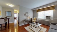 This well-appointed single-floor residence offers a thoughtfully arranged layout that balances comfort and style. The living room serves as the heart of the home, showcasing rich hardwood flooring, wainscoting along the walls, and a large window dressed with bold gold-and-grey striped Roman shades that allow natural light to fill the space. A classic cast-iron radiator, a mirrored accent console table, and a sleek glass-top coffee table contribute to the room's elegant yet inviting ambiance. The kitchen features warm natural wood cabinetry, granite-style countertops, a gas range, and a window that brings in additional natural light, creating a practical and pleasant cooking environment. The bedroom is a serene retreat with hardwood flooring, a window with natural light, a cast-iron radiator, and a warm, welcoming atmosphere accentuated by coral tones. The full bathroom is finished with neutral ceramic floor tiles, full-surround wall tiling in the tub area, and a window above the tub that provides ventilation and light. Throughout the residence, a cohesive neutral color palette ties each room together, creating a harmonious and comfortable living environment.