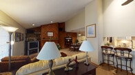 This single-floor residence offers a thoughtfully designed layout that balances open communal spaces with private accommodations. The living room serves as a central gathering area, featuring vaulted ceilings that lend a sense of spaciousness, soft carpeting, and a ceiling fan overhead. The space flows naturally toward the dining area, which is distinguished by a striking diagonal wood-paneled accent wall, a pendant light fixture, and room for a full dining set—creating a warm, inviting atmosphere for entertaining.

Adjacent to the dining area, the kitchen is equipped with white appliances, including a range and over-the-range microwave, complemented by honey-toned wood cabinetry that provides ample storage. The open sightlines between the kitchen and dining room enhance the overall connectivity of the living spaces.

Both bedrooms are carpeted and comfortably sized. One bedroom features French doors that invite natural light and provide outdoor access. The shared full bathroom includes a tub-shower combination, a wood-framed vanity with a wide countertop, and tile flooring. Throughout the residence, warm wood tones and neutral walls create a cohesive, comfortable aesthetic.