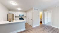 This single-floor residence offers a well-designed, open layout with a cohesive aesthetic throughout. The kitchen serves as a functional centerpiece, featuring white shaker-style cabinetry extending to the upper walls, bright white countertops, and a full suite of stainless steel appliances including a refrigerator, electric range, and over-the-range microwave. A peninsula extends from the kitchen, providing additional counter space and defining the transition into the living area. Wood-look luxury vinyl plank flooring runs continuously through the kitchen and main living spaces, lending warmth and a sense of flow.

The living area is generously sized, bathed in natural light through a large sliding glass door fitted with vertical blinds that opens to an outdoor patio. A secondary entry door is also accessible from this space. Neutral warm-beige walls complement the flooring throughout. The bedroom is a calm, comfortable space featuring plush carpeting and a window with outdoor views, allowing natural light to fill the room.

The bathroom is clean and straightforward, featuring a tub-shower combination with a curtain rod, wood-look flooring, and crisp white fixtures. Multiple closet doors along the hallway provide ample storage throughout the unit.