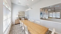 This 230 square foot conference room in Chattanooga, TN, showcases a perfect blend of functionality and modern aesthetics. The space is dominated by a large, solid wood table that comfortably seats up to ten people, complemented by white, slat-back chairs. Overhead, a distinctive geometric pendant light fixture adds visual interest and provides focused illumination.

Natural light floods the room through expansive windows equipped with adjustable blinds, creating a bright and airy atmosphere. The walls are painted in a crisp white, enhancing the sense of spaciousness. A contemporary abstract artwork adorns one wall, adding a touch of sophistication.

The room features a variety of lighting options, including recessed ceiling lights and a sleek, linear pendant light above the table. A stylish console with a chevron pattern stands against one wall, offering additional storage or display space. The floor is covered with a textured, neutral-toned carpet that adds warmth and helps with acoustics.

Adjacent areas visible through glass partitions suggest this is part of a larger, open-concept office space. The overall design emphasizes clean lines and a minimalist approach, creating an environment conducive to productive meetings and collaborative work sessions.