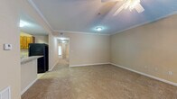 This single-floor residence offers two bedrooms and two full bathrooms within a thoughtfully laid-out floor plan. The living area features warm neutral tones, plush carpeting, and crown molding, with a ceiling fan adding a functional accent. A set of French doors floods the space with natural light and provides access to an outdoor area.

The kitchen is well-appointed with rich, dark-stained wood cabinetry offering generous storage, light granite-style countertops, and a full suite of black appliances including a range, over-the-range microwave, and refrigerator. Light ceramic tile flooring completes the kitchen's practical design.

Both bathrooms are finished with tile flooring and dark wood vanities topped with light countertops. One bathroom includes a tub-shower combination, while the second features a vanity with ample drawer and cabinet storage beneath a large wall mirror.

The bedrooms are carpeted and neutral in tone, with one featuring access to a spacious walk-in closet outfitted with multi-level wire shelving for organized storage. Throughout the unit, consistent warm beige walls and white trim create a cohesive, clean aesthetic.