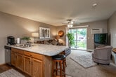 This single-floor residence offers a thoughtfully designed layout that balances comfort and functionality throughout. The open-concept living area is anchored by plush carpeting, a ceiling fan with light fixture, and a large sliding glass door that fills the space with natural light while providing direct access to a private patio overlooking a green outdoor setting. A granite-topped breakfast bar with bar seating connects the living room seamlessly to the kitchen, creating an inviting space for both relaxing and entertaining.

The kitchen is outfitted with warm oak cabinetry, stainless steel appliances including a range, over-the-range microwave, and refrigerator, complemented by a decorative tile backsplash and durable hardwood-style flooring. Generous counter space and ample storage make this an efficient and practical cooking area.

The bedrooms are carpeted and feature ceiling fans, natural light from well-positioned windows, and warm neutral tones. The primary bedroom includes a walk-in closet and direct access to a private en-suite bathroom. An additional full bathroom serves the remainder of the residence, finished with tile flooring, an oak vanity, and a shower-tub combination. Throughout, the warm color palette and consistent use of wood-toned finishes create a cohesive and welcoming atmosphere.