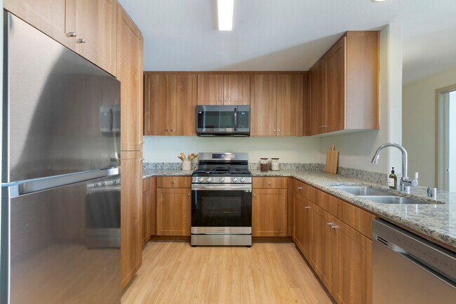 Cocina renovada del Paquete I con gabinetes de roble, encimeras de granito moteado beige, electrodomésticos de acero inoxidable y pisos de superficie dura. - Avalon San Dimas