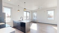 Located at 2040 N Hillcrest Pkwy in Altoona, Wisconsin, this efficiently designed single-floor studio offers a thoughtfully planned open-concept layout. The space features light hardwood-style flooring throughout, clean white walls, and navy blue baseboards that add a contemporary accent.

The kitchen is a standout feature, anchored by a large island with a waterfall-edge quartz countertop, an undermount sink with a matte black faucet, and dark wood-tone cabinetry. Stainless steel and black appliances — including a refrigerator, range, and over-the-range microwave — are complemented by a tile backsplash and matching upper cabinets. Stylish globe pendant lights illuminate the workspace.

The open living area receives generous natural light through multiple windows, offering views of the surrounding Altoona landscape. A ceiling fan provides year-round comfort, and a wall-mounted HVAC unit ensures climate control. Panel-style interior doors with matte black hardware add a modern touch throughout.

The bathroom is clean and minimal, featuring light wood-tone cabinetry with a quartz countertop, a soaking tub with tiled surround, a tall frosted window for natural light and privacy, and hardwood-style flooring that maintains design continuity with the rest of the space.