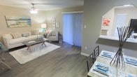 This single-floor residence offers a thoughtfully designed open-concept layout that seamlessly connects the living and dining areas, creating a comfortable and functional flow throughout the space. The living area features smooth hardwood-style flooring in a warm, neutral tone that extends throughout the main living space, adding a sense of cohesion and warmth. A ceiling fan with a light fixture overhead provides both practical ventilation and ambient lighting. The living room is centered around a cozy seating arrangement, complemented by a soft area rug and accented by tasteful wall art and a decorative lamp. Natural light pours into the space through a large sliding glass door dressed with vertical blinds, offering a bright and airy atmosphere. The dining area, positioned adjacent to the living space, features a dining table with classic chairs and a set of coordinated place settings, making it ideal for everyday meals or casual entertaining. The neutral wall tones throughout create a calm, inviting backdrop that works well with a variety of décor styles. A small display shelf adds a charming architectural detail to one wall. Overall, this space combines practical design with welcoming aesthetics for comfortable single-level living.