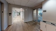 Located at 420 East Ohio Street in Chicago's Streeterville neighborhood, this professional office space is thoughtfully designed to maximize functionality within a compact single-floor footprint. The layout is anchored by two hallways that serve as the connective spine of the space, guiding occupants through a clean, modern environment.

The corridors are finished with warm-toned hardwood flooring that runs continuously throughout, creating a cohesive and inviting atmosphere. Recessed lighting and a drop-tile ceiling provide consistent, even illumination across the space. Along the hallways, frameless glass-panel partitions with brushed stainless steel hardware divide individual work areas, offering both visual openness and a sense of privacy. The frosted and textured glass panels add a refined, contemporary touch while maintaining an airy feel.

The private office areas visible from the hallways are accented with warm earth-tone walls and feature standing desks, monitor setups, and curated wall art, reflecting a productive yet comfortable work environment. A seating nook along one corridor — complete with a cushioned bench and a large-format black-and-white artwork — offers a moment of pause and artistic character. A glazed door at one end of the hallway reveals an adjacent fitness area, hinting at a broader, amenity-rich facility. The overall ambiance is polished, professional, and well-appointed.