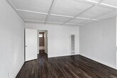 Located in the East Hollywood neighborhood of Los Angeles, this single-floor unit at 1014 N Oxford offers a thoughtfully designed layout with a clean, modern aesthetic throughout. The main living area is immediately distinguished by a striking coffered ceiling with beadboard detailing, painted bright white to maximize the sense of openness and height. Dark hardwood-style flooring runs consistently throughout, providing a warm contrast to the crisp white walls. Natural light filters generously through horizontal-slatted window blinds, casting patterned light across the floors and lending the space an airy, inviting atmosphere. A wall-mounted A/C unit and a vertical heating unit ensure year-round comfort. The open kitchen is well-appointed with white shaker cabinetry, light quartz countertops, a classic white subway tile backsplash, and stainless steel appliances including a gas range, microwave, and refrigerator. A ceiling fan overhead adds both function and charm to the adjoining dining or living area. The bedroom offers a quiet, neutral retreat with its own window framing an outdoor view. The bathroom is finished with large-format textured tile, a soaking tub, glass shower enclosure, and a small window for natural ventilation—combining practicality with a contemporary spa-like feel.