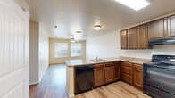 This single-story residence is designed with a practical, open layout that connects the kitchen and living areas seamlessly. The kitchen serves as a central hub, featuring rich dark wood cabinetry with ample upper and lower storage, granite-style countertops, and black appliances including a range, dishwasher, and refrigerator. A peninsula with a double sink and breakfast bar overhang extends into the living space, enhancing functionality and flow. Wood-style flooring runs consistently throughout the unit, lending a cohesive, clean aesthetic.

The living and dining areas benefit from natural light provided by multiple windows fitted with blinds, and ceiling fans are installed in key rooms to support comfort year-round. The textured ceilings add subtle dimension throughout the main living spaces.

The bedrooms are well-proportioned, each featuring a ceiling fan, a window with exterior views, and the same wood-style flooring. The bathroom is cleanly appointed with a full tub-shower combo, a dark wood vanity with a granite-style countertop, and matching flooring. A dedicated in-unit laundry area houses a full-size washer and dryer alongside a water heater, adding everyday convenience to this efficiently organized home.
