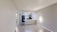 This well-designed one-bedroom, one-bathroom unit offers a practical and comfortable single-floor layout. The open-concept living and kitchen area serves as the heart of the space, featuring durable hardwood-style plank flooring throughout. The kitchen is equipped with black appliances, including a refrigerator, electric range with overhead exhaust, and dishwasher, complemented by gray cabinetry and a white speckled countertop that extends into a peninsula — ideal for casual dining or additional prep space. The living area is bright and neutral, with wall-mounted sconce lighting and a window unit providing climate control, while a front-facing window allows natural light to fill the room. A hallway connects the living space to the private areas of the unit. The bedroom is carpeted for comfort and features a window with blinds that brings in natural light, alongside wall sconce lighting. A dedicated closet provides convenient storage. The bathroom includes a tub/shower combination with white tile surround, a speckled vanity countertop, and wood-style flooring. Throughout, neutral gray tones and textured ceilings contribute to a clean, understated aesthetic.