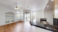 This 710 square foot apartment offers a well-designed living space with a single bedroom and bathroom. The open-plan layout maximizes the available area, combining the kitchen, living, and dining spaces seamlessly. The kitchen boasts honey-colored wood cabinets, black appliances, and a stylish blue-tiled backsplash, complemented by dark countertops. A central island with a breakfast bar divides the kitchen from the living area, enhancing functionality.

The living room features warm wood flooring and a built-in entertainment center with shelving, adding character and storage. Large windows and a sliding glass door leading to a balcony flood the space with natural light, offering views of palm trees and the surrounding area. Ceiling fans throughout provide comfort and air circulation.

The bedroom, measuring 140 square feet, includes a closet and is equipped with a ceiling fan. The bathroom, while compact, appears functional with a shower/tub combination. A separate laundry room with full-sized washer and dryer adds convenience.

The apartment's neutral color palette, predominantly white walls, creates a bright, airy atmosphere that complements the wood flooring. This efficient layout maximizes the use of space, making it an ideal residence for singles or couples seeking a modern, low-maintenance living environment.