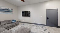 Located at 116 E Randolph Ave in Enid, Oklahoma, this modern 2-bedroom, 2-bathroom unit offers a thoughtfully designed single-floor layout with a clean, contemporary aesthetic throughout. The open-concept living and kitchen area serves as the heart of the space, featuring polished concrete-style flooring, neutral gray walls, and bold dark baseboards that add a sleek, urban edge. The kitchen is well-appointed with white shaker-style cabinetry, a full suite of stainless steel appliances including a refrigerator, range, microwave, and dishwasher, and a striking white center island with bar seating illuminated by stylish black pendant lights. The adjoining living room provides a comfortable gathering space with a ceiling fan and a wall-mounted TV. Both bedrooms offer a calm, restful atmosphere with plush light-colored flooring, ceiling fans, built-in closets with panel doors, and large windows that frame urban views of the surrounding Enid cityscape, allowing for ample natural light. The bathrooms are finished in a clean, bright palette featuring marble-look tile flooring, a single-sink vanity with white countertop, and a frameless sliding glass shower enclosure with brushed nickel fixtures. The overall design balances modern functionality with a refined, minimalist style.