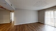 This single-floor unit offers a practical and functional layout across two bedrooms and two bathrooms. Wood-look flooring runs throughout the living areas and bedrooms, providing a cohesive aesthetic, while neutral gray walls and white trim create a clean, understated interior palette. Textured ceilings are present throughout the unit.

The living area is generously proportioned, featuring a sliding glass door that allows natural light to filter in and provides access to an outdoor space. The front entry opens directly into this living area, with a hallway connecting to the rest of the unit.

The kitchen is equipped with white cabinetry, a white electric range, an under-cabinet range hood, and light-toned countertops. Light wood-look flooring continues into this space.

Both bedrooms feature ceiling fans with light fixtures, wood-look flooring, and neutral walls. The primary bedroom is a well-sized room with access to a dedicated closet. The second bedroom receives natural light through a window with blinds.

The two bathrooms each feature wood-look flooring and light countertops. One bathroom includes a walk-in shower, while the second is fitted with a tub-shower combination.