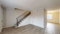 This two-story home offers a well-organized layout across both levels, connected by a carpeted staircase with a classic black metal railing. The main floor features durable wood-look vinyl flooring throughout the living and dining areas, with neutral-toned walls and textured ceilings that lend a clean, understated aesthetic. The kitchen is a functional highlight, equipped with white shaker cabinetry, granite-style countertops, a peninsula with an integrated sink, and black appliances including a range and refrigerator. A pendant light and a large window brighten the adjacent dining area, creating a welcoming space for everyday meals. The upper level hosts the bedrooms, each finished with plush carpet, ceiling fans with light fixtures, and windows fitted with blinds that allow for natural light and privacy. One room features a sliding glass door with vertical blinds opening to an outdoor area. The bathrooms are tastefully appointed with white vanities, granite-style countertops, wood-look flooring, and tiled tub-shower combinations. Throughout the home, consistent finishes and a neutral color palette create a cohesive and comfortable living environment suited for a variety of lifestyles.