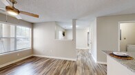This single-floor residence offers a thoughtfully designed layout that balances open communal spaces with comfortable private retreats. The living area greets you with warm wood-look luxury vinyl flooring, neutral warm-toned walls, and a textured ceiling, all complemented by a ceiling fan and a door that invites natural light from outside. A distinctive half-wall pass-through with a small shelf connects the living space to adjacent areas, adding architectural interest while maintaining an open feel.

The galley-style kitchen is well-equipped, featuring white shaker cabinetry, granite-look countertops, black appliances including a refrigerator, range, and dishwasher, and a double-basin stainless steel sink. Wood-look flooring continues throughout, tying the space together cohesively.

The bedrooms are carpeted for comfort. One bedroom benefits from a large window that frames views of greenery outside, paired with a ceiling fan for year-round comfort. A spacious walk-in closet with wire shelving and hanging rods provides generous storage. The bathroom offers a white vanity with granite-look counters, a large mirror with bright overhead lighting, and wood-look tile flooring. The overall ambiance is clean, modern, and move-in ready.