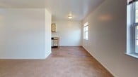 This single-floor, two-bedroom unit features a straightforward, functional layout designed for comfortable everyday living. The living area is generously sized, finished with neutral-toned carpeting and clean white walls that create a bright, open atmosphere. A front entry door opens directly into this space, which also benefits from a wall-mounted heating unit and a window that draws in natural light. The adjoining dining area transitions seamlessly into the kitchen, where wood-look hard flooring provides a practical surface underfoot. The kitchen is equipped with white cabinetry, a white electric range, a refrigerator, a dishwasher, and a stainless steel sink, along with overhead cabinetry offering ample storage. Both bedrooms are carpeted and feature white walls, with windows that allow natural light to filter in. One bedroom includes two closets — one standard and one walk-in — providing notable storage capacity. The bathroom is outfitted with a full tub and shower combination featuring a clean white surround and chrome fixtures. Throughout the unit, the consistent use of neutral tones and clean finishes contributes to a simple, well-maintained aesthetic.