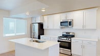 This well-designed three-story home offers a functional and modern layout across its multiple levels. The ground floor provides an attached garage with an automatic opener and a concrete floor, offering convenient parking and additional storage space. An entrance leads up carpeted staircases with clean white railings connecting each level of the home.

The main living floor features an open-concept kitchen and living room with light hardwood-style flooring and recessed lighting. The kitchen is outfitted with white shaker cabinetry, white quartz countertops, a central island with a sink, and stainless steel appliances including a gas range, microwave, and refrigerator — a practical and stylish setup for everyday cooking.

The upper floor houses both bedrooms, each finished with plush carpeting and windows fitted with blinds that allow natural light to filter in. The primary bedroom is a comfortable size and offers outdoor views. A dedicated closet with built-in shelving and a window provides organized storage. Both bathrooms are finished with tile flooring, white vanities with quartz countertops, and subway tile surrounds in the bathtub areas, complemented by modern light fixtures. A hallway connects the upper-floor rooms, completing this well-appointed multi-level home.